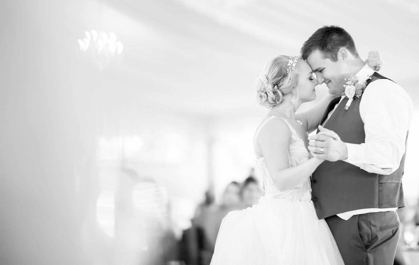 Braut und Bräutigam tanzen einen romantischen ersten Tanz, berühren sich sanft an der Stirn und lächeln. Ein eleganter Veranstaltungsort mit Kronleuchtern sorgt für die richtige Stimmung, während ein HochzeitsDJ für Franken und Thüringen den perfekten Soundtrack für ihren besonderen Moment liefert.