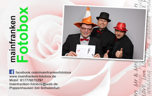 Drei Männer in Anzug und Fliege posieren für ein Foto, jeder trägt einen anderen bunten Hut. Der Hintergrund zeigt eine große Rosengrafik und die Kontaktdaten von mainfranken Fotobox - perfekt für jede fränkische Veranstaltung oder wenn Sie einen Hochzeits-DJ brauchen!.