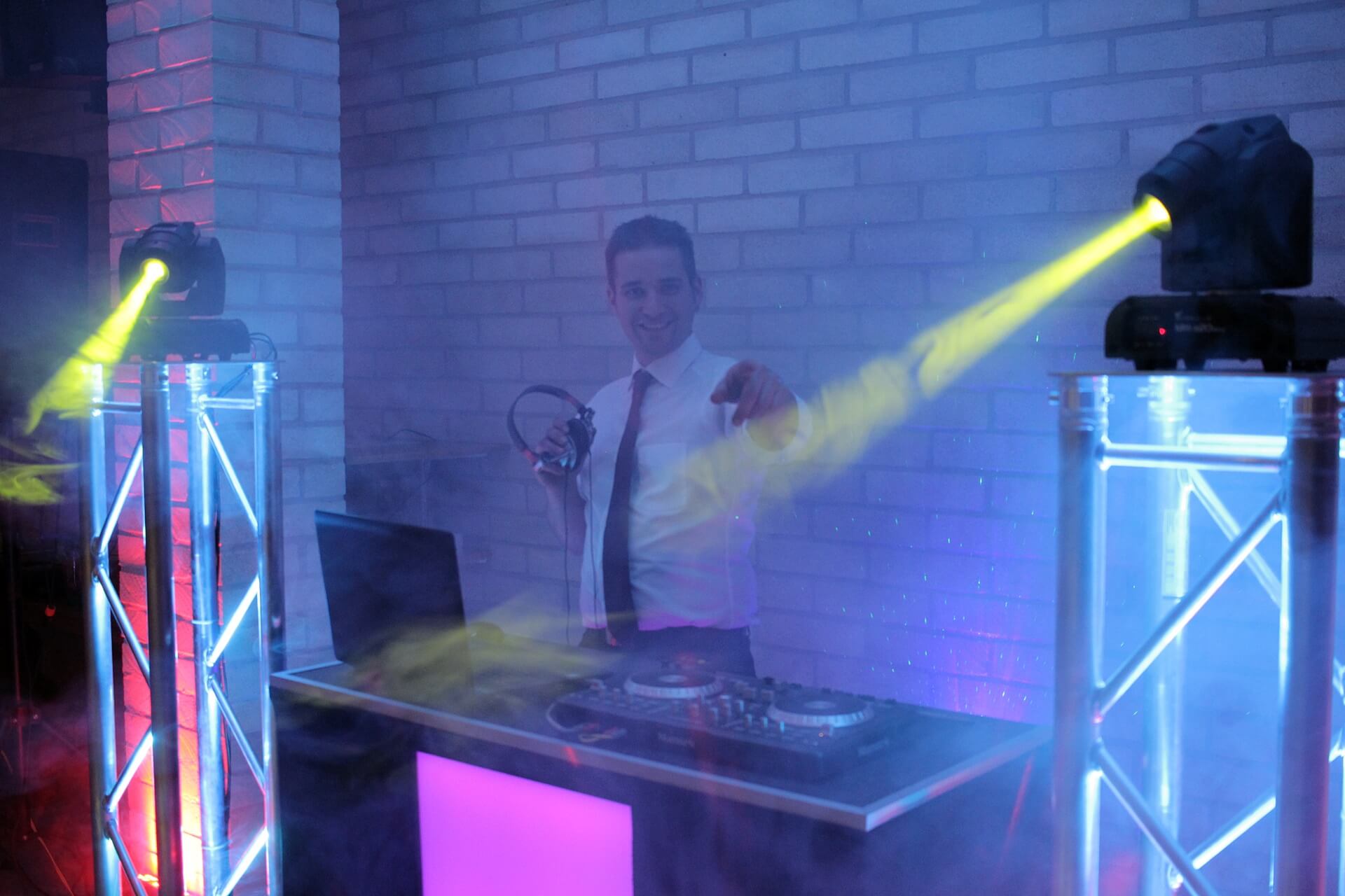 Hochzeits DJ in Franken und Thüringen ❤️ Die DJs mit der Roten Fliege ❤️ Ein DJ für Hochzeit in weißem Hemd und Krawatte steht lächelnd hinter dem Mischpult, hält Kopfhörer und genießt die bunten Lichter und Nebeleffekte - die perfekte Stimmung mit Ihrem Hochzeits DJ aus Thüringen.