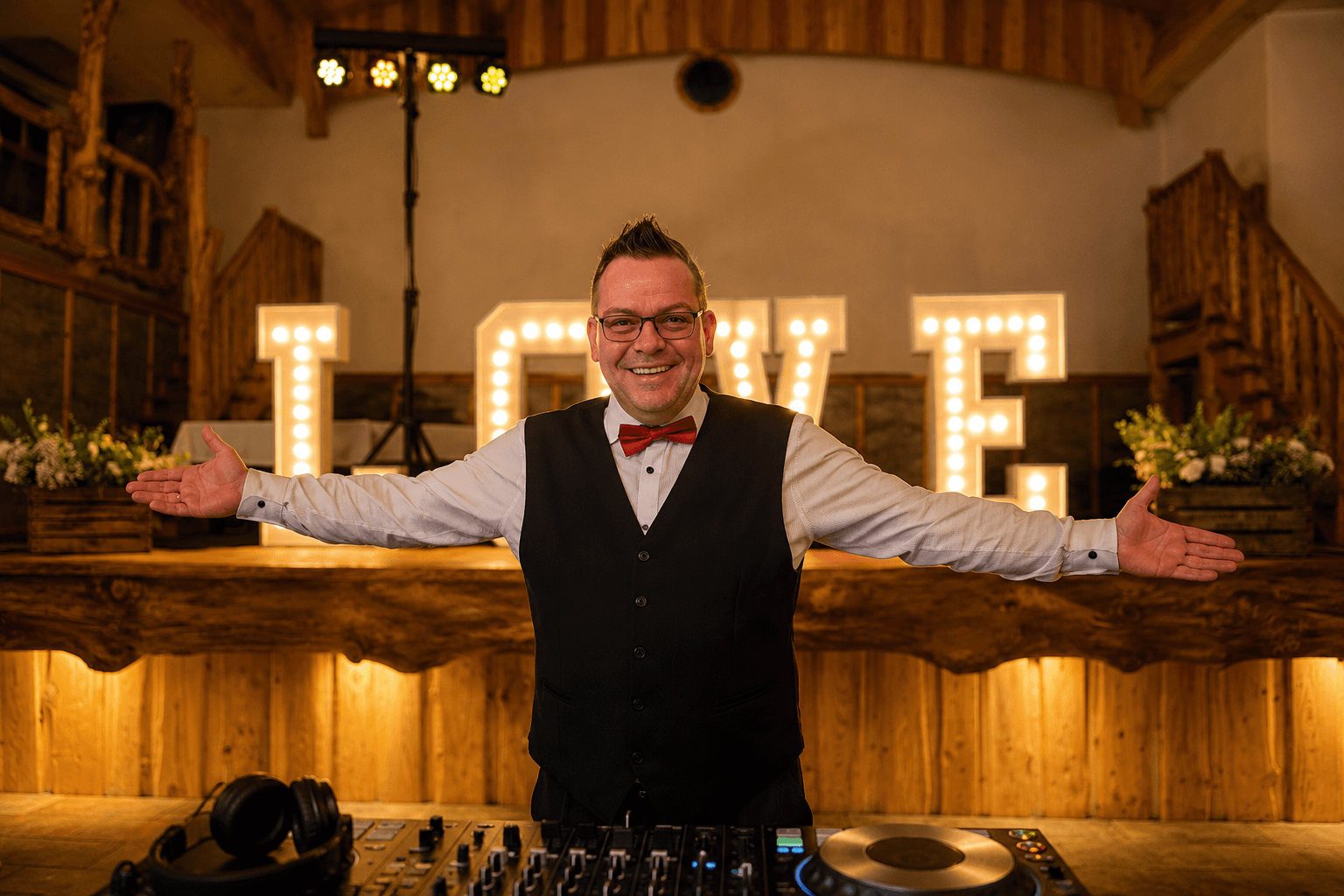 Hochzeits-DJ mit roter Fliege vor beleuchtetem LOVE-Schriftzug